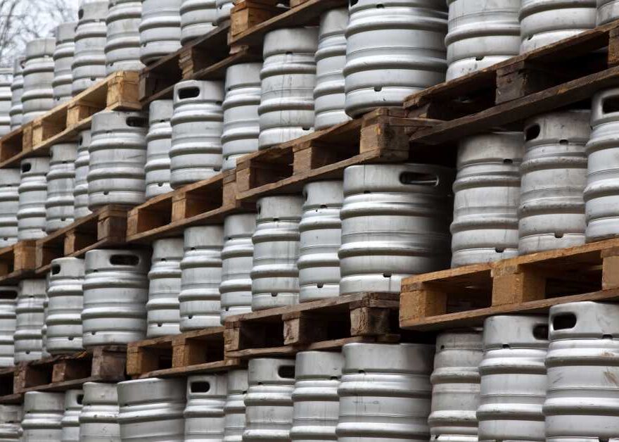 Rows of metal beer kegs are stacked on wooden pallets outdoors, forming a large organized storage area.